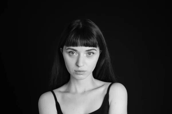 Studio portrait of a pretty brunette woman in a black spaghetti strap top, looking at the camera, against a plain black background