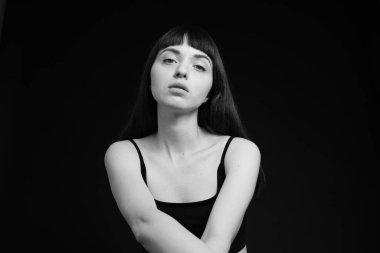 Siyah spagetti askılı güzel esmer bir kadının stüdyo portresi, düz siyah bir arka planda, kameraya bakıyor.