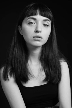 Siyah spagetti askılı güzel esmer bir kadının stüdyo portresi, düz siyah bir arka planda, kameraya bakıyor.