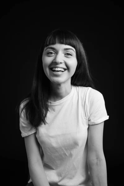 Studio portrait of a pretty brunette woman in a white blank t-shirt, against a plain black background, looking at the camera