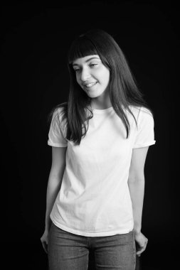 Beyaz tişörtlü, esmer bir kadının stüdyo portresi. Siyah bir arka plana bakıp gülümsüyor.