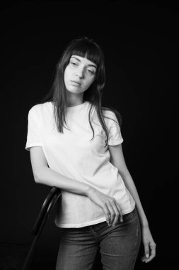 Beyaz, boş tişörtlü esmer bir kadının stüdyo portresi, düz siyah bir arka plan, yan bakan