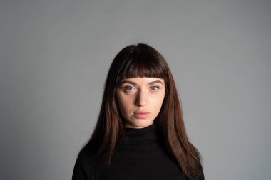 Güzel esmer bir kadının stüdyo portresini kapat, katlanmış siyah polo yaka kazak giyen, kameraya bakan, düz gri bir arka plan