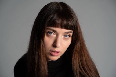 Güzel esmer bir kadının stüdyo portresini kapat, kameraya bak, düz gri bir arka planda.