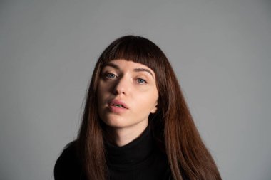 Güzel esmer bir kadının stüdyo portresini kapat, kameraya bak, düz gri bir arka planda.