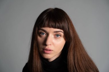 Güzel esmer bir kadının stüdyo portresini kapat, kameraya bak, düz gri bir arka planda.