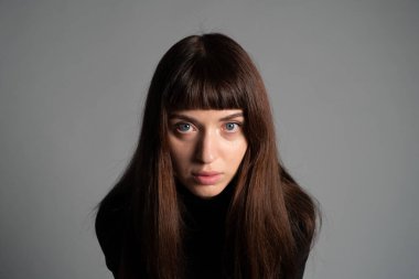 Güzel esmer bir kadının stüdyo portresini kapat, kameraya bak, düz gri bir arka planda.