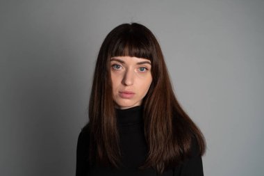 Güzel esmer bir kadının stüdyo portresini kapat, kameraya bak, düz gri bir arka planda.