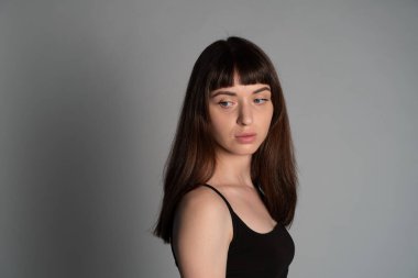 Siyah spagetti askılı güzel esmer bir kadının stüdyo portresi, ciddi ciddi yana bakıyor, düz gri bir arka plan karşı yarı dönmüş