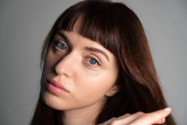 Güzel esmer bir kadının stüdyo portresini kapat, kameraya bak, düz gri bir arka planda.