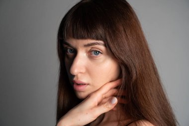 Güzel esmer bir kadının stüdyo portresini kapat, el yanağında, kameraya bakıyor, yarı dönüş, düz gri bir arka plan