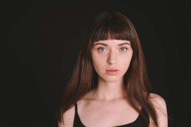 Siyah spagetti askılı güzel esmer bir kadının stüdyo portresi, düz siyah bir arka planda, kameraya bakıyor.