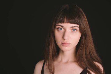 Siyah spagetti askılı güzel esmer bir kadının stüdyo portresi, düz siyah bir arka planda, kameraya bakıyor.