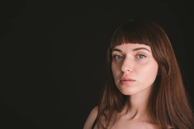 Siyah spagetti askılı güzel esmer bir kadının stüdyo portresi, düz siyah bir arka planda, kameraya bakıyor.