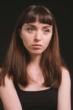 Siyah spagetti askılı güzel esmer bir kadının stüdyo portresini kapat, düz siyah bir arka plana bakıyor.