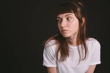 Beyaz, boş tişörtlü, siyah arka planda kameraya bakan esmer bir kadının stüdyo portresi.