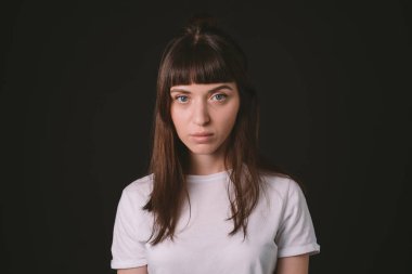 Beyaz, boş tişörtlü esmer bir kadının stüdyo portresi, düz siyah bir arka planda, ciddi ciddi kameraya bakıyor.