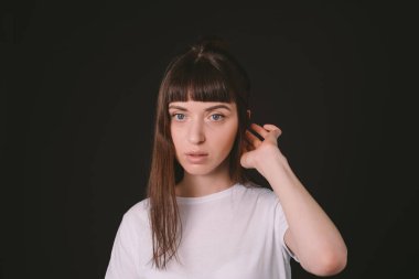 Beyaz, boş tişörtlü esmer bir kadının stüdyo portresi, düz siyah bir arka planda, ciddi ciddi kameraya bakıyor.