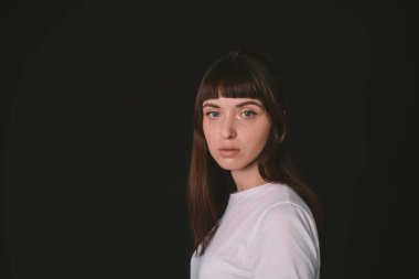 Beyaz, boş tişörtlü, siyah arka planda kameraya bakan esmer bir kadının yan görüntüsü.