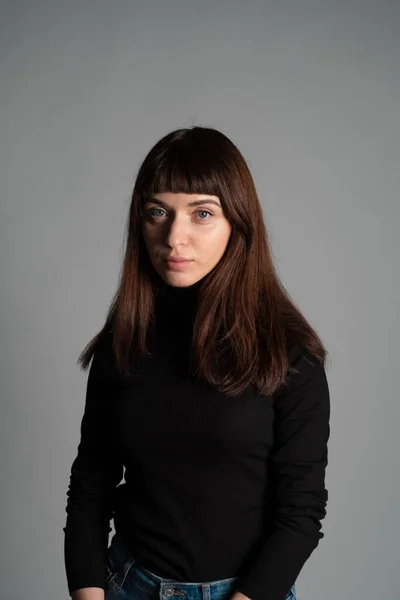工作室的肖像一个漂亮的黑发女人 穿着折叠的黑色圆领毛衣 看着相机 面对着一个普通的灰色背景 — 图库照片