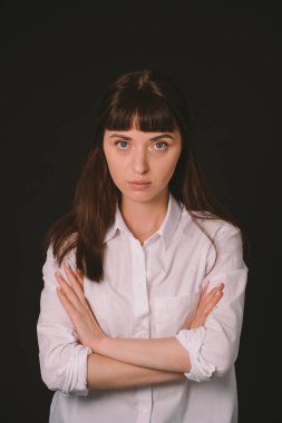 Beyaz gömlekli güzel esmer bir kadının stüdyo portresi düz siyah bir arka planda, kameraya bakıyor.