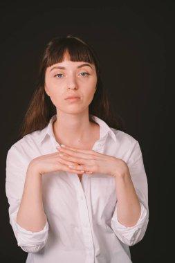 Beyaz gömlekli güzel esmer bir kadının stüdyo portresi, düz siyah bir arka plan üzerinde, el ele tutuşarak, kameraya bakarak