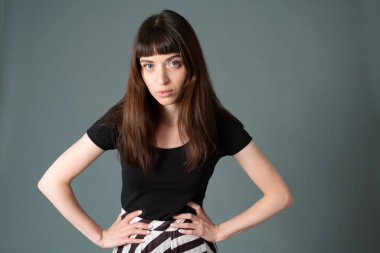 Siyah tişörtlü güzel esmer bir kadının stüdyo portresi, düz gri bir arka planda kameraya bakıyor.