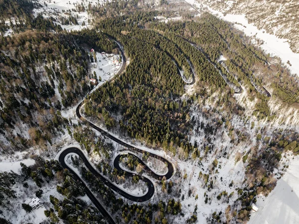 Winding road from high mountain pass, in winter time. Aerial view by drone . Romania