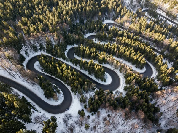 Winding road from high mountain pass, in winter time. Aerial view by drone . Romania