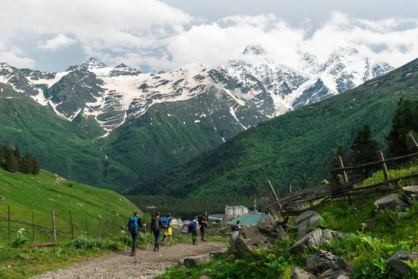 Gevarieerde groep jonge mensen mannen en vrouwen lopen op bergpad naar dorp. — Stockfoto