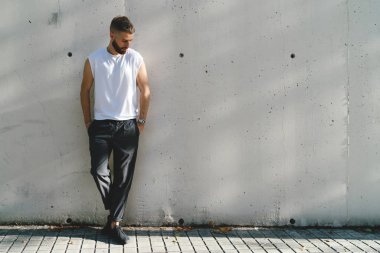 Sakallı hippi adam boş beyaz tişört giymiş bir cadde üzerinde beyaz bir arka plan üzerinde dururken aşağıya bakıyor. Şık adam elinde bir güneşli gün açık havada cepler ile ayakta.