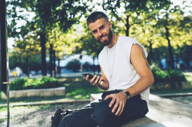 Açık havada otururken yakışıklı sakallı hippi adamın Smartphone kullanarak wifi bağlantısı 