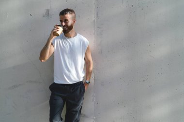 Başarılı genç zevk sabah kahve beyaz duvar arka plan üzerinde duran adam. Sakallı hippi bir kenara gülümseyen gitmek boş bir beyaz t-shirt bir kahve ile 