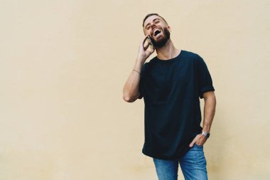 Bir sokakta bir cep telefonuyla konuşurken gülüyor boş siyah t-shirt giyen öğrenci adam 