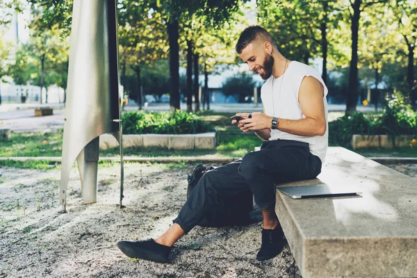 都市庭のベンチに座りながら携帯電話を使用して若い男の笑みを浮かべてください — ストック写真