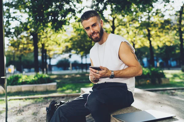 Smartphone kullanarak rahat kıyafetler içinde gülümseyen yetenekli blogger. Yeni müşteri e-posta cevap için genç adam manifatura mesaj üstünde hareket eden telefon.