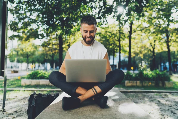 ハンサムな若者の肖像画彼の膝にラップトップを屋外に座ってノート パソコンのキーボードに入力男性ひげを生やした — ストック写真