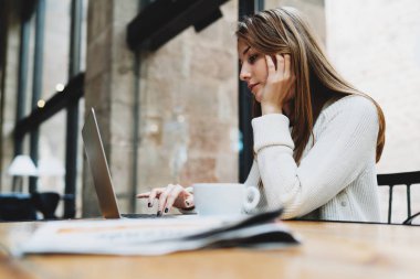 Bir kafede otururken dizüstü bilgisayar ile çalışan genç kadın