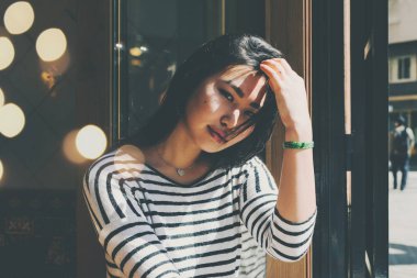 Yarım uzunlukta saç el ile bir kafede otururken dokunmadan süre kameraya bakarak gündelik kıyafeti giymiş uzun siyah saçlı dalgın bir rüya gibi Asya kadın portresi 