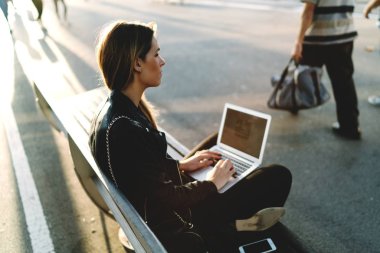 Şık erkek dizlerinin üstünde a laptop ile Street bir bankta oturmuş sarı saçlı. Wifi internet açık havada için yan görünüm taşınabilir bir bilgisayarda çalışan bir kadının fotoğrafını bağlı.