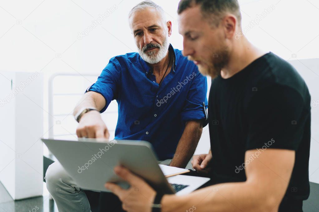 Two bearded men wearing smart casual clothes discussing business strategy of the company by analyzing information in annual company report browsed on a portable computer from the internet.