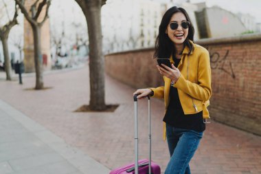 Genç, gülümseyen bir kadın gezgin, yeni bir şehirde ilk dakikalarının tadını çıkarıyor ve duygularını bir akıllı telefonla online olarak arkadaşlarıyla paylaşıyor. Asyalı hippi kız cep telefonundan mesaj okuyor..