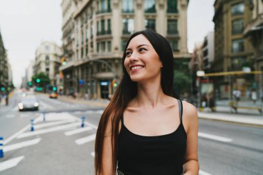 Genç, güzel, beyaz bir model şehrin arka planında dikilirken kameraya poz veren modaya uygun kıyafetler giyen bir kadın. Şık bir turist kız hafta sonu gezisi boyunca şehirde gezmekten zevk alıyor.. 