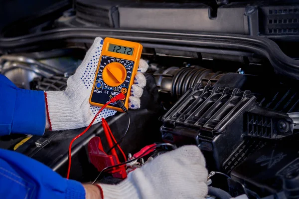 Car electrical equipment repair. Measuring instrument in digital value. Accumulator voltage measurement. Monitoring the health of the car. Part of the photo is blurry.