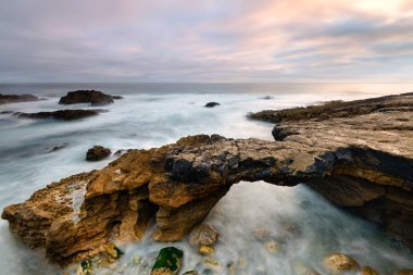 Cascais Portekiz deniz manzarası. Gelgit tarafından oyulmuş taş köprü. Lizbon yakınındaki kıyı manzara. Fırtınalı bir günde uzun pozlama.