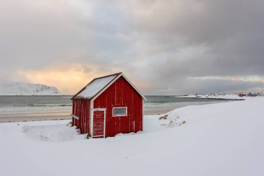 Norveç 'teki Lofoten Adaları ve gün batımındaki güzel kış manzaraları. Karla kaplı plajda kırmızı evi olan Idyllic manzarası. Kuzey Kutup Dairesi 'nde turistik cazibe.