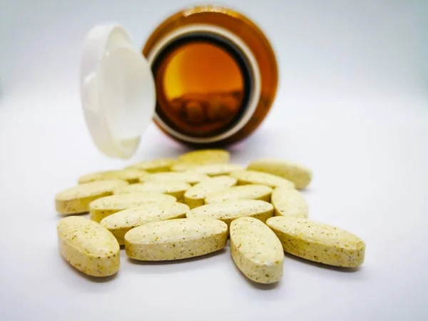 İlaç ve sağlık kavramı. Ayrıca vitamin eksiklikleri (vitamin eksikliği) tedavi etmek için kullanılan birçok oval sarı tablet multivitamin. Orada cam şişeden döktü. Beyaz arka plan, seçici odak ve kopya alanı izole.