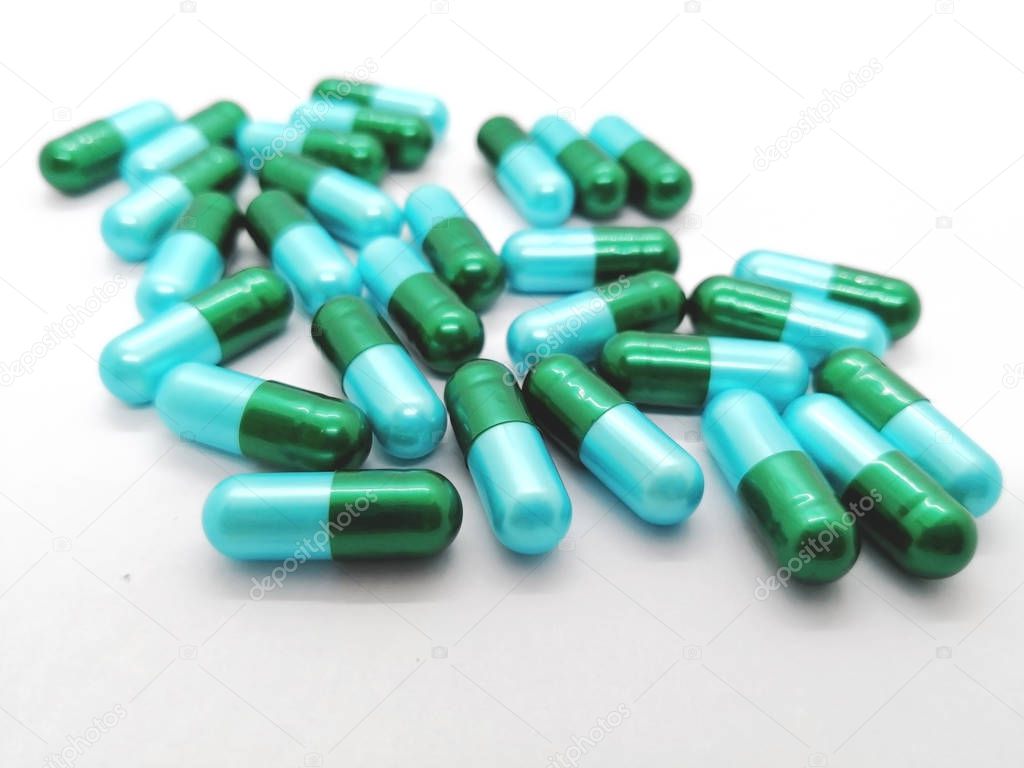 Medication and healthcare concept. Many green-blue capsules of Amoxicillin 500 mg. isolated on white background, used to treat many different types of infection caused by bacteria. Focus on foreground and copy space.