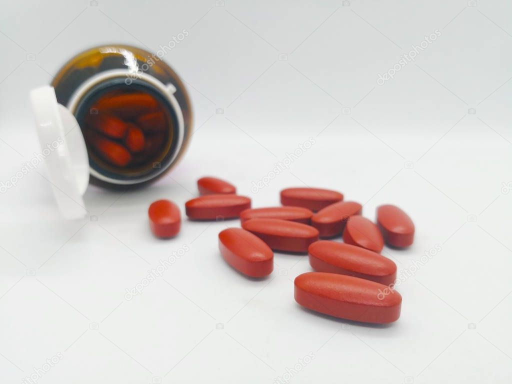 Medication and healthcare concept. Many oval brown tablets of multivitamin, that are also used to treat vitamin deficiencies (lack of vitamins). There were poured out of glass bottle. Isolated on white background and copy space.