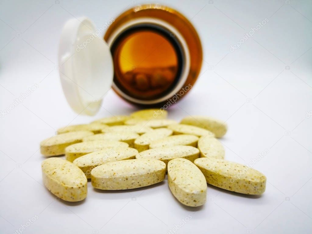 Medication and healthcare concept. Many oval yellow tablets of multivitamin, that are also used to treat vitamin deficiencies (lack of vitamins). There were poured out of glass bottle. Isolated on white background, selective focus and copy space.